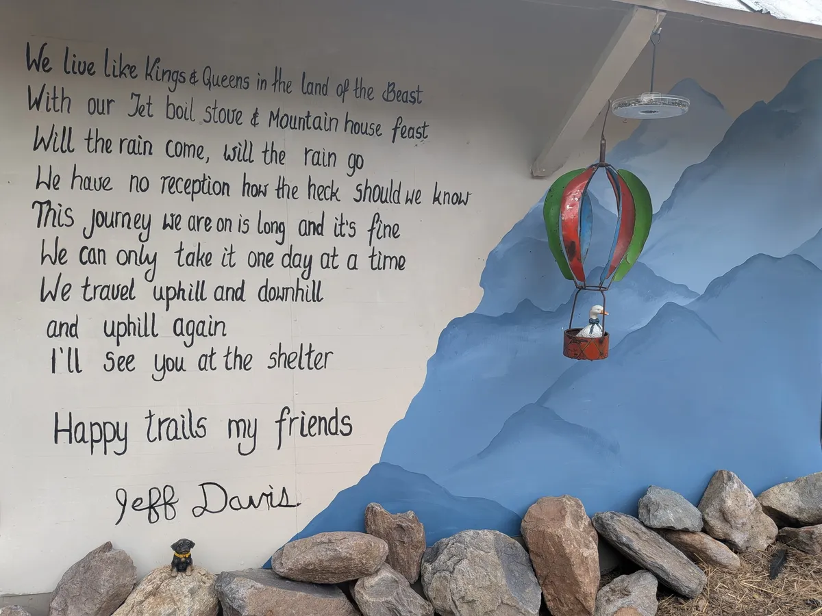 Close-up of Jeff Davis's hand-painted Ode to the AT mural — the full poem written in black against painted blue mountains, with a hot air balloon hanging in front