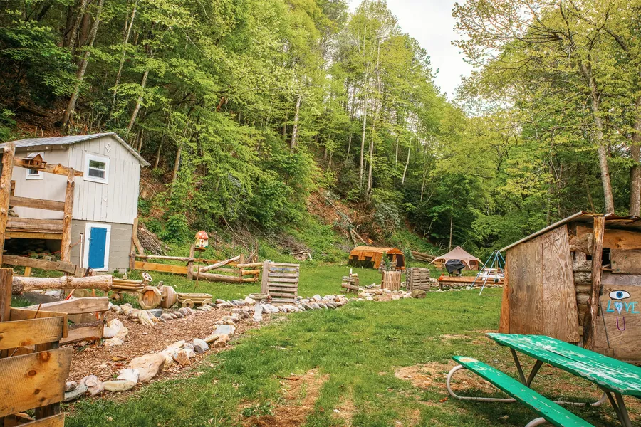 Tent pitches in the grass at the edge of the treeline, with the mountains rising behind